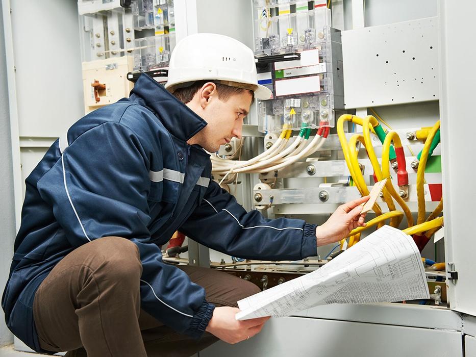 Technician checking switchboard drawings and schedules against the installed assembly